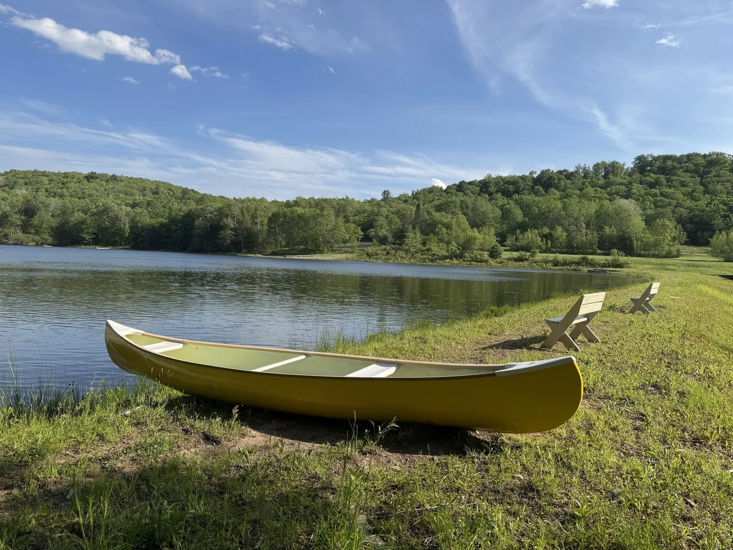 Yellow canoe on the shore of the private lake at Verdant Sound — lakeside benches and forested Catskills hills
