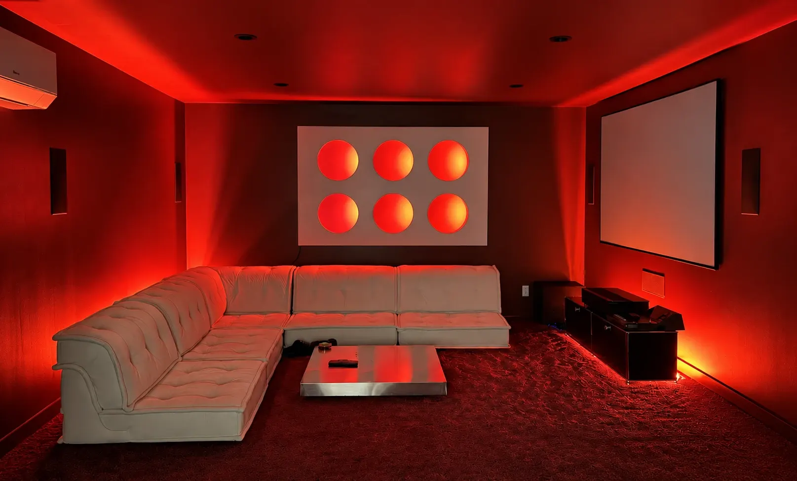 Verdant Sound subterranean theater — red LED accent lighting, cream sectional, illuminated circular shelves, and a large projection screen